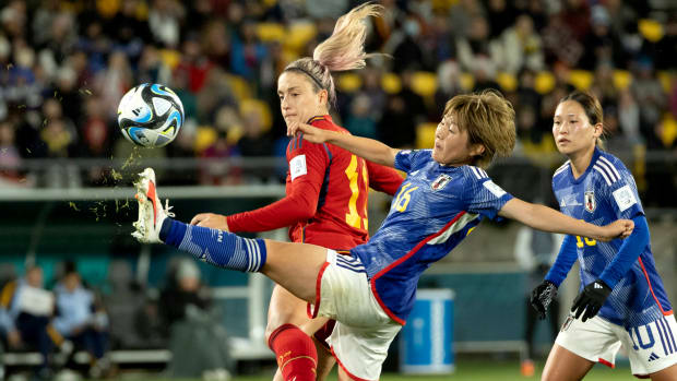 Grass flies from Japan's Honoka Hayashi's boot as she stretches to make a waist high kick behind Spain's Alexia Putellas at the Women's World Cup.